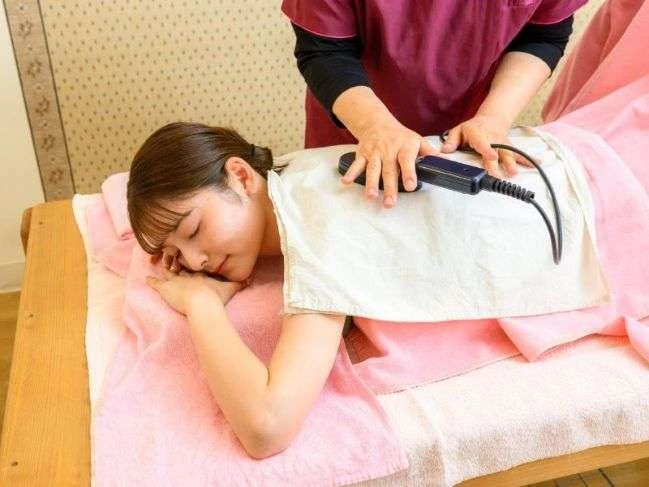 琉球温熱療法の施術風景。女性の背中を優しく温めている様子